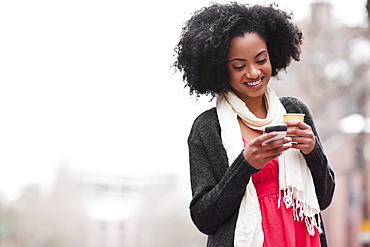 USA, Washington State, Seattle, Cheerful young woman text messaging while holding takeaway coffee