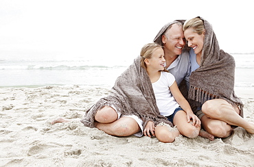 Smiling parents with daughter (10-11) on coastline covered by blanket