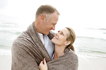 Embraced couple covered by blanket looking each other