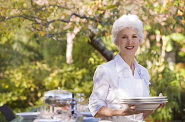 Senior woman standing in garden holding stack of plates