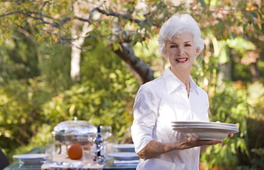 Senior woman standing in garden holding stack of plates