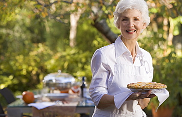 Senior woman standing in garden holding plate with pie