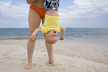 Mother holding baby boy upside-down on beach