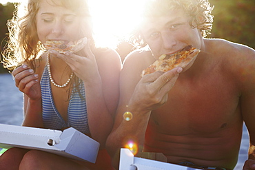 Young couple eating pizza on beach