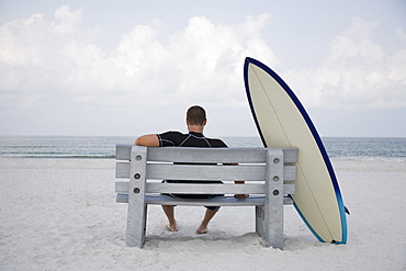 Surfer sitting on bench next to surfboard