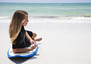 Girl listening to mp3 player on surfboard, Florida, United States