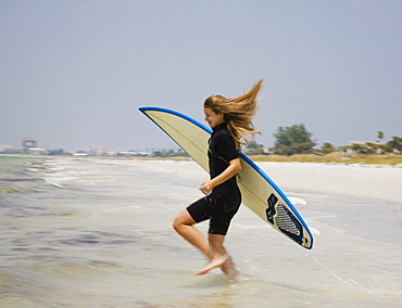 Girl running into water with surfboard, Florida, United States