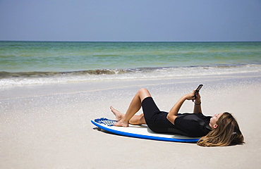 Girl looking at cell phone on surfboard, Florida, United States