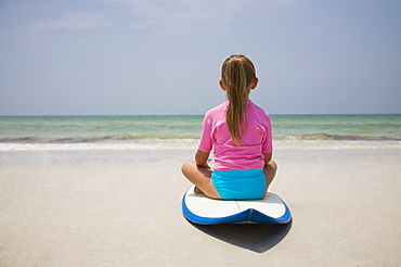 Young girl sitting on surfboard, Florida, United States