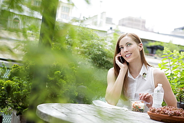 Portrait of young woman sitting on balcony and using mobile phone, New York City, USA