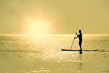 Man standing on paddle board at sunset