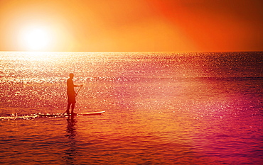 Man standing on paddle board at sunset