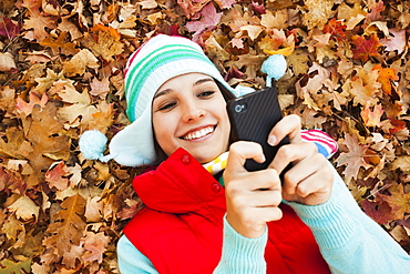 Young woman lying on autumn leaves and using 