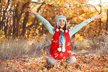 Happy young woman sitting on autumn leaves in forest, Alpine, Utah