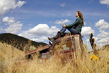 USA, Colorado, Woman resting on roof of abandoned truck in desert