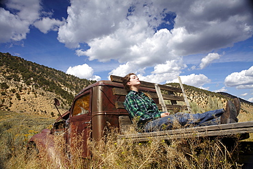 USA, Colorado, Woman resting on bed of abandoned truck in desert