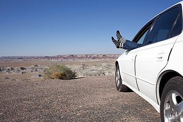 USA, Arizona, Winslow, Woman sticking feet out of car window parked in desert