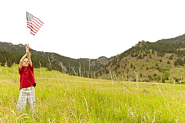 Boy (6-7) waving American flag in meadow