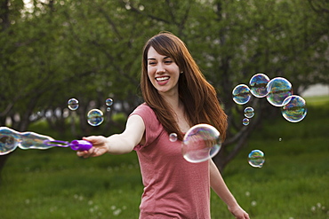 Young woman blowing bubbles in orchard