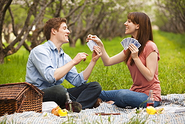 USA, Utah, Provo, Young couple playing cards during picnic in orchard