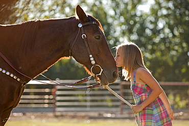 Cowgirl (8-9) kissing horse in ranch