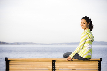 Portrait of woman relaxing on bench near sea