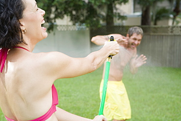 Woman spraying man with hose in backyard