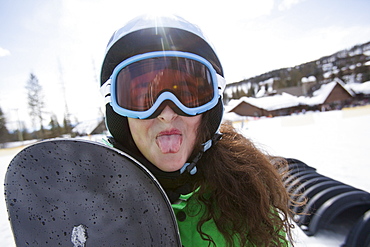 Girl with snowboard sticking out her tongue, USA, Montana, Whitefish