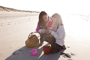 Mother with daughter collecting shells on beach