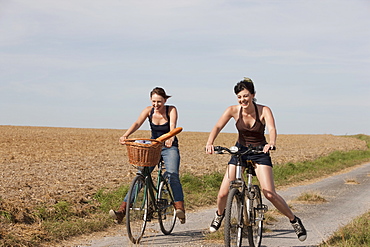 France, Picardie, Albert, Young women on bikes on country road, France, Picardie, Albert