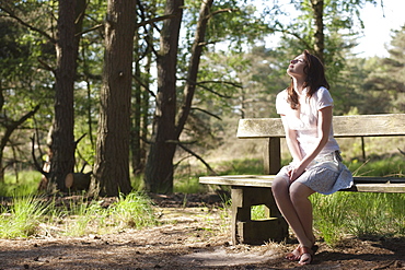 Belgium, Kalmthoutse Heide, Young woman sitting on bench, Kalmthoutse Heide (near Antwerpen), Belgium
