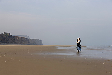 France, Pas-de-Calais, Escalles, Young woman strolling on empty beach, France, Pas-de-Calais, Escalles