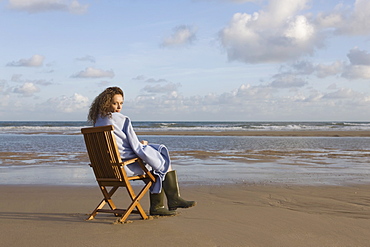 France, Pas-de-Calais, Escalles, Young woman sitting on chair on empty beach, France, Pas-de-Calais, Escalles