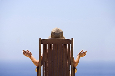 Spain, Costa Blanca, Rear view of woman sitting on wooden chair, facing sea