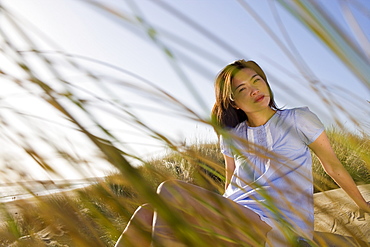 USA, California, Point Reyes, Young woman sitting in grass on sand dune