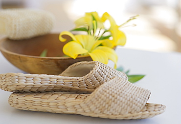 Slippers beside a wooden bowl with yellow lilies in it