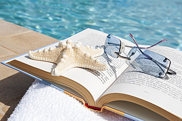 Book and sunglasses by swimming pool