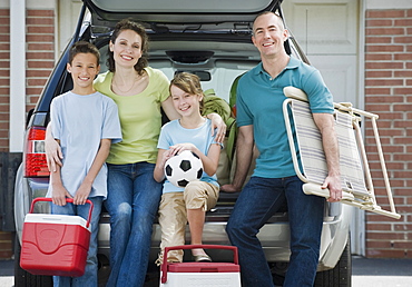 Family holding coolers and beach chair behind car