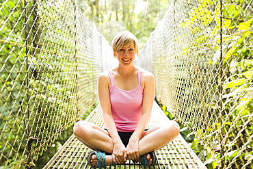 Woman sitting with legs crossed and smiling to camera on footbridge in forest, Costa Rica