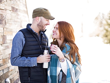 Mid adult couple looking face to face and having drink from vacuum flask