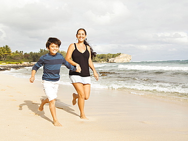 Boy (10-11) running on beach with mother, Kauai, Hawaii