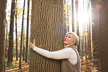 USA, New Jersey, Smiling woman hugging tree in Autumn forest