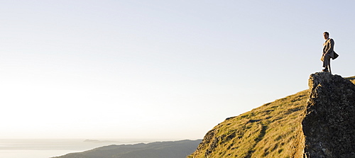 Businessman standing on rock overlooking ocean