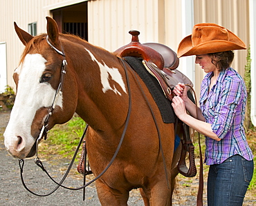 Woman putting saddle on horse