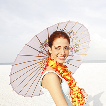 Young woman posing on beach with lei and umbrella