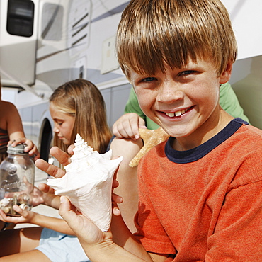 Children looking at seashell collection by motor home