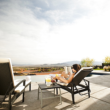 Young attractive woman reading book by swimming pool, USA, Utah, St. George