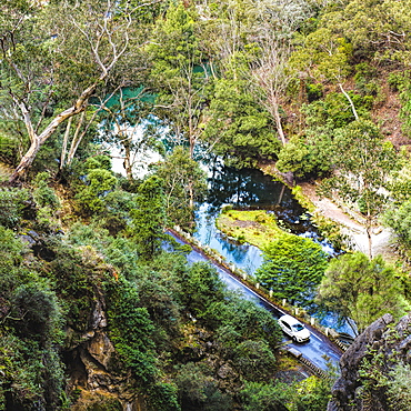 Australia, New South Wales, Jenolan Caves, Blue Lake, Car on road at shore of lake among forest covered slopes