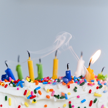 Extinguished birthday candles on cake - one still burning