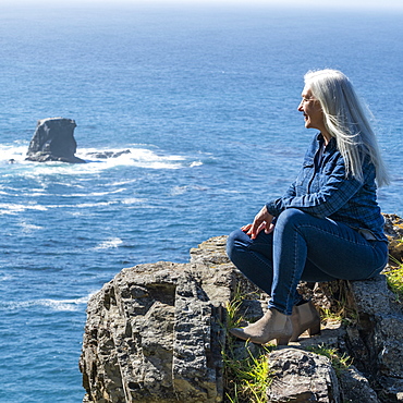 USA, California, Big Sur, Woman sitting at the edge of cliff looking at view